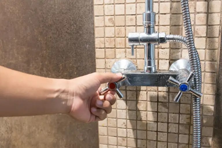 A hand turning the hot-water valve of their shower in Lakeway, Texas.