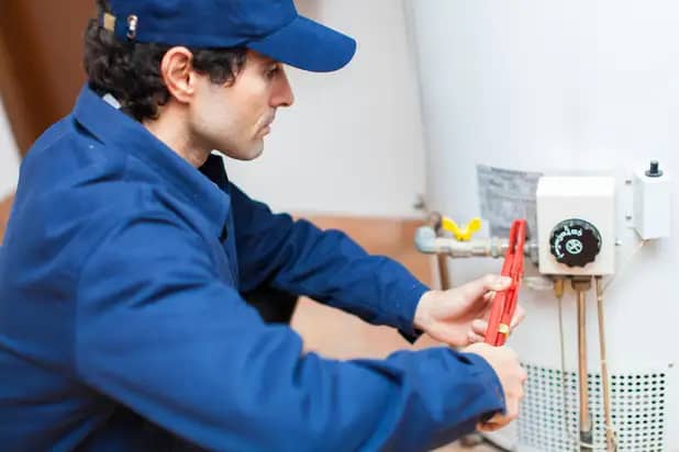 A plumber using a wrench to repair a tank style hot water heater in Bee Caves TX.