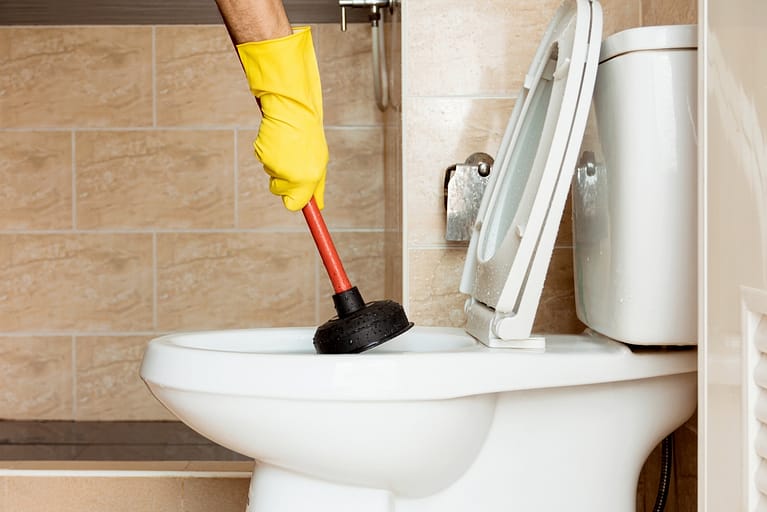 Side view of a hand using a plunger to unclog a toilet in Austin, TX.