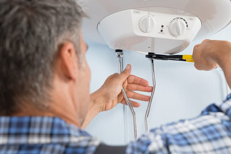 A licensed plumber using a wrench to fix a tankless water heater in Leander, TX.