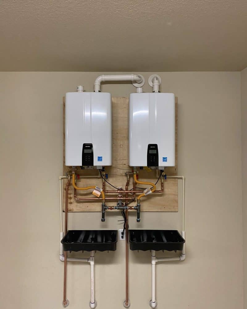 Two Navien tankless water heaters installed with associated pipes and drip pan